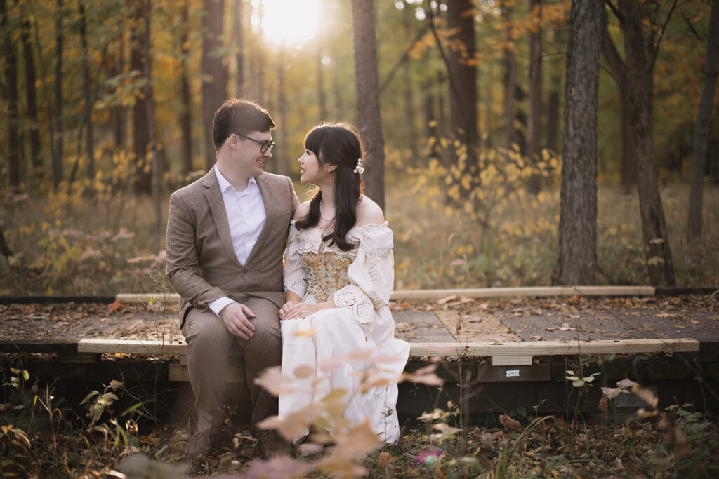 Engagement photo session at Busey Woods featuring a couple sitting on a boardwalk surrounded by forest and golden evening light in Urbana, Illinois.