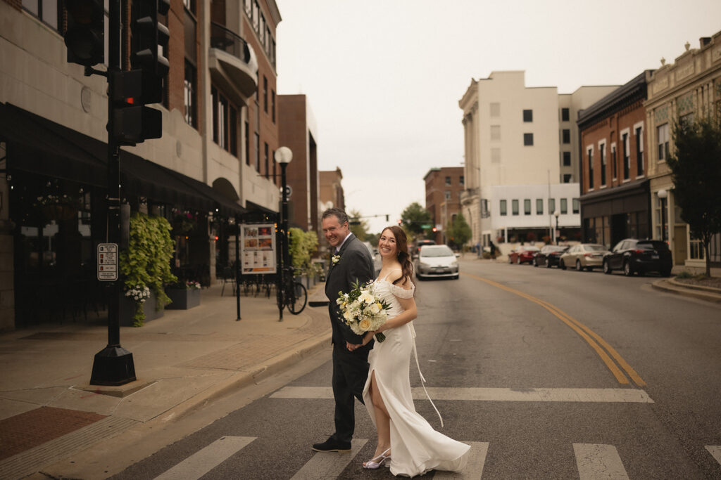 Bride and groom crossing a downtown Champaign street during their wedding portrait session in Champaign, Illinois.