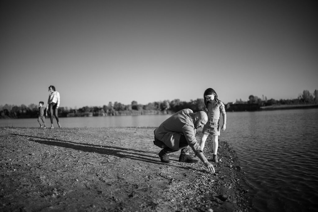 Father and daughter skipping stones by the water during a candid family photography session at Lake of the Woods in Mahomet, Illinois.