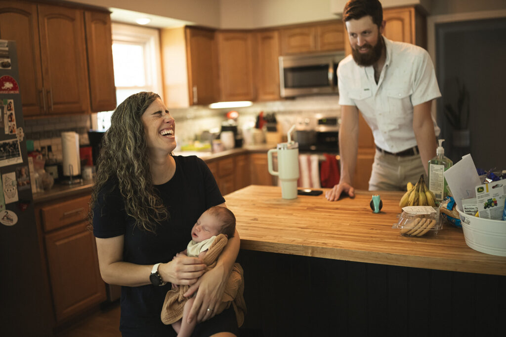 Mother holding her newborn baby and sharing a joyful moment with her husband during an in-home family photography session in Champaign-Urbana.