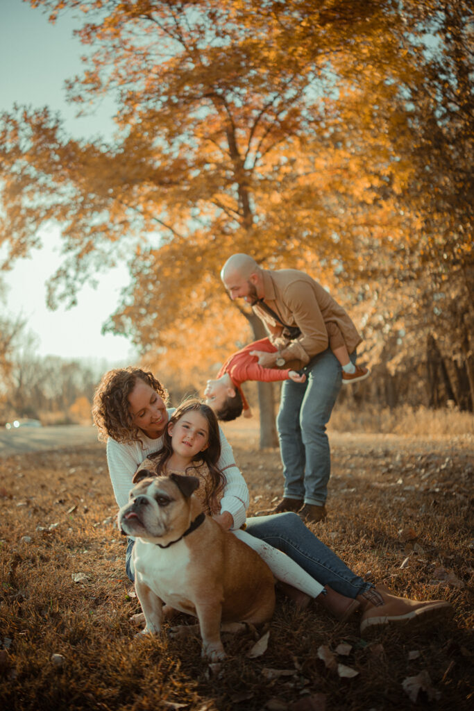 Parents with two young children and a bulldog sitting together in a scenic, fall setting at River Bend in Mahomet, IL, photographed by Light By Zoey Photography, Champaign, IL.