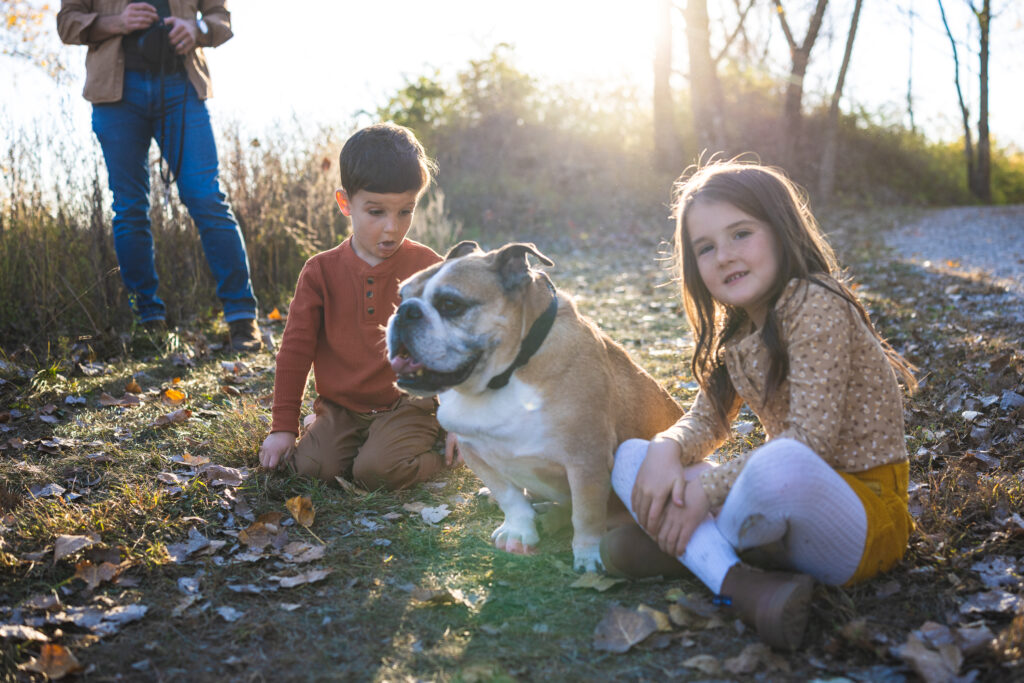 Young girl hugging a bulldog with a big smile at River Bend in Mahomet, IL during a family photo session with Light By Zoey Photography, Champaign, IL