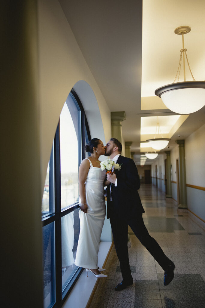 Newlyweds sharing a kiss by the courthouse window after their Champaign County courthouse wedding in Urbana, Illinois.