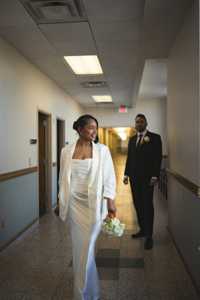 Bride walking through the courthouse hallway while the groom follows behind after their wedding ceremony in Urbana, Illinois.